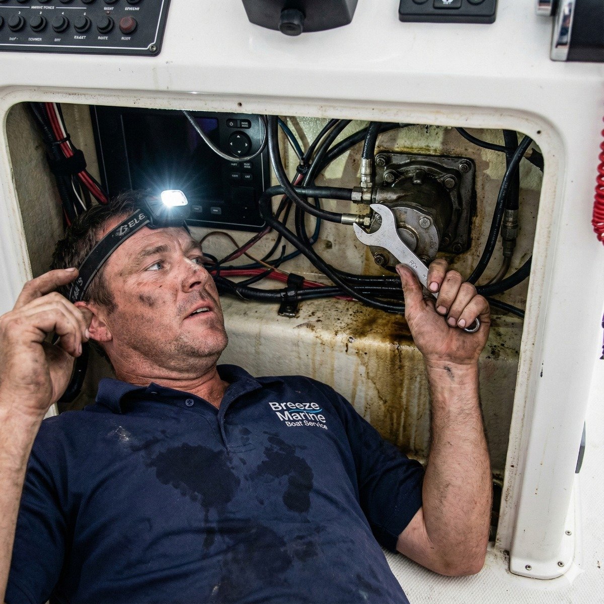 Marine technician working under a boat console, using a specialized wrench to remove a leaking SeaStar hydraulic steering helm pump for a seal replacement.